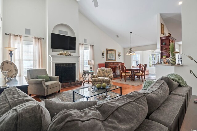 living room with high vaulted ceiling, wood-type flooring, a fireplace, and an inviting chandelier