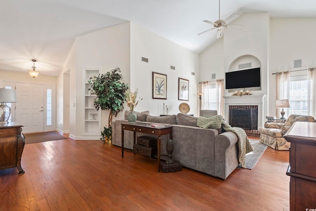 living room with hardwood / wood-style flooring, ceiling fan, a fireplace, built in features, and high vaulted ceiling