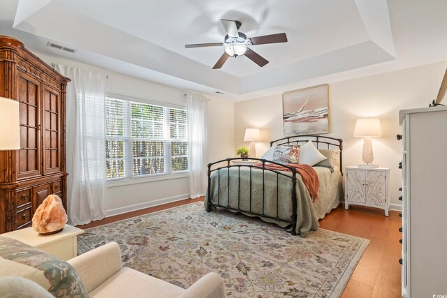 bedroom with ceiling fan, light hardwood / wood-style flooring, and a tray ceiling