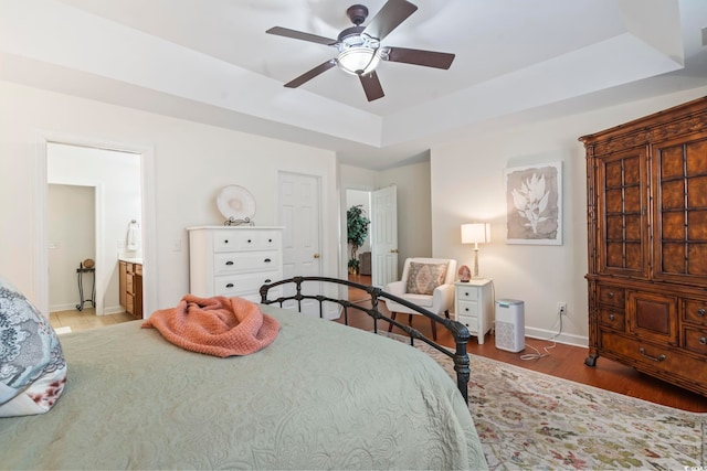 bedroom with a raised ceiling, ceiling fan, connected bathroom, and light hardwood / wood-style floors