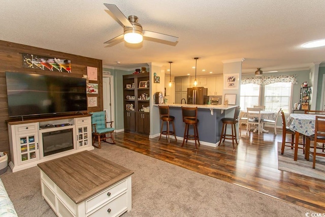 living room featuring a textured ceiling, dark wood-type flooring, ornamental molding, and ceiling fan