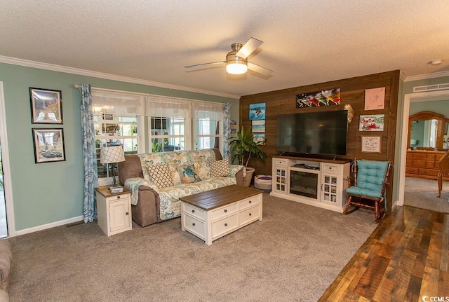 carpeted living room featuring a textured ceiling, ceiling fan, wooden walls, and crown molding