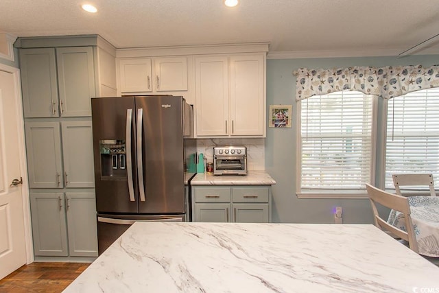 kitchen with light stone counters, ornamental molding, stainless steel fridge with ice dispenser, and a healthy amount of sunlight