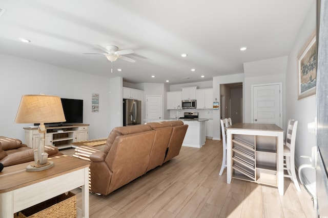 living room featuring ceiling fan, light wood-type flooring, and sink