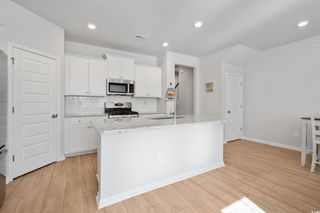 kitchen with appliances with stainless steel finishes, sink, white cabinetry, and an island with sink