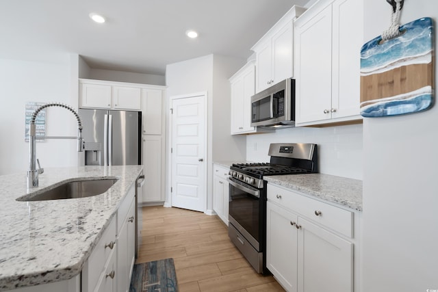 kitchen with tasteful backsplash, sink, light hardwood / wood-style flooring, appliances with stainless steel finishes, and white cabinets