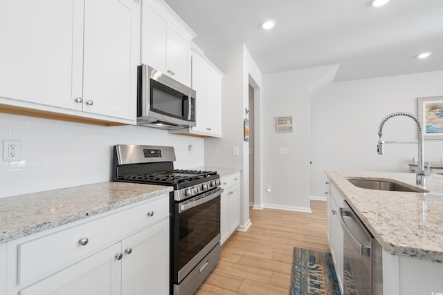 kitchen featuring tasteful backsplash, sink, light stone countertops, stainless steel appliances, and white cabinets