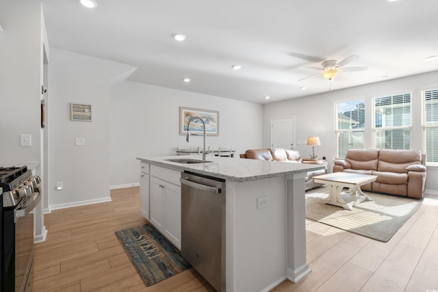 kitchen featuring a center island with sink, sink, white cabinetry, light stone countertops, and stainless steel appliances