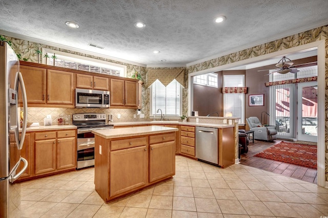 kitchen featuring a textured ceiling, stainless steel appliances, light tile patterned floors, a kitchen island, and ceiling fan