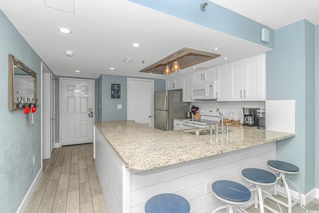 kitchen featuring light wood-type flooring, light stone counters, white appliances, a peninsula, and white cabinets