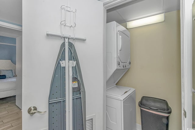 laundry room featuring stacked washer / drying machine, wood finished floors, and laundry area