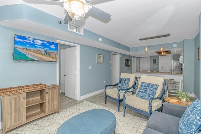 living area featuring a ceiling fan, visible vents, light wood finished floors, and baseboards