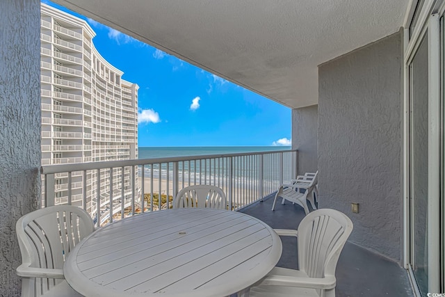 balcony with outdoor dining area, a water view, and a view of the beach