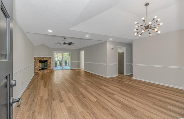 unfurnished living room with a stone fireplace, ceiling fan with notable chandelier, lofted ceiling, a textured ceiling, and light hardwood / wood-style flooring