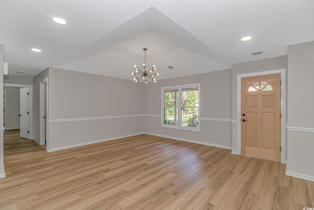 foyer entrance with lofted ceiling, a chandelier, a textured ceiling, and light wood-type flooring