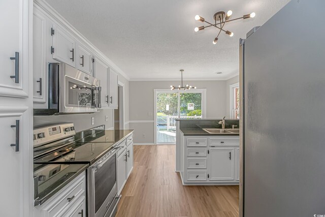 kitchen with sink, light wood-type flooring, appliances with stainless steel finishes, a notable chandelier, and white cabinets