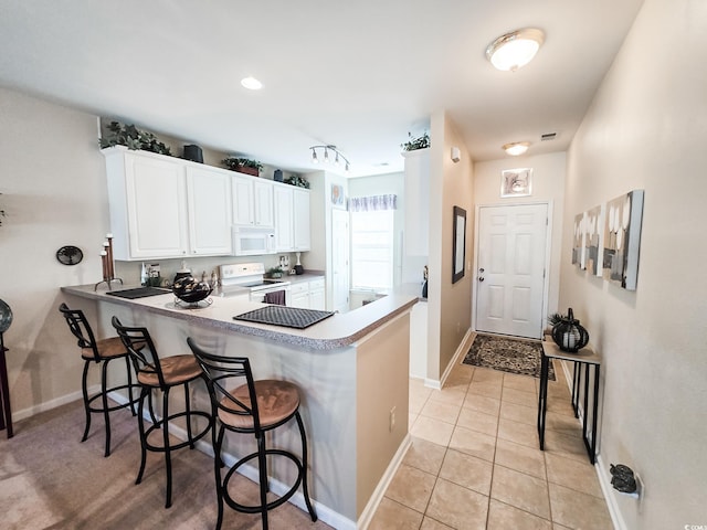 kitchen with white appliances, white cabinetry, a kitchen bar, and kitchen peninsula