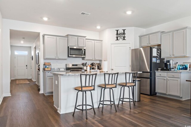 kitchen with appliances with stainless steel finishes, an island with sink, gray cabinets, and dark hardwood / wood-style floors