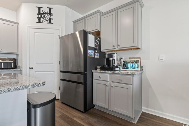 kitchen with dark wood-type flooring, stainless steel refrigerator, light stone counters, and gray cabinets