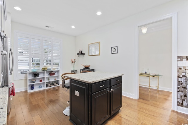 kitchen featuring light stone countertops, a kitchen island, stainless steel fridge, and light wood-type flooring