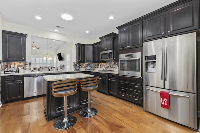 kitchen featuring stainless steel appliances, a kitchen bar, decorative backsplash, and light wood-type flooring