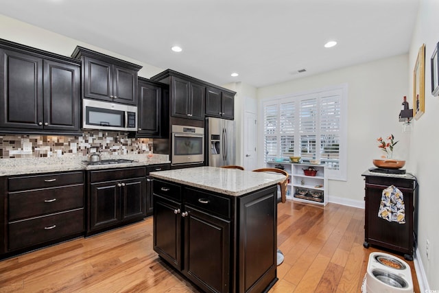 kitchen with appliances with stainless steel finishes, backsplash, a center island, light stone counters, and light wood-type flooring