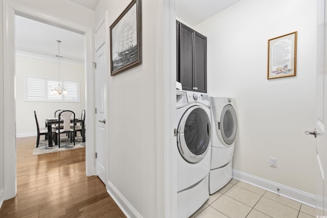 laundry room with cabinets, ornamental molding, light tile patterned floors, washing machine and clothes dryer, and an inviting chandelier