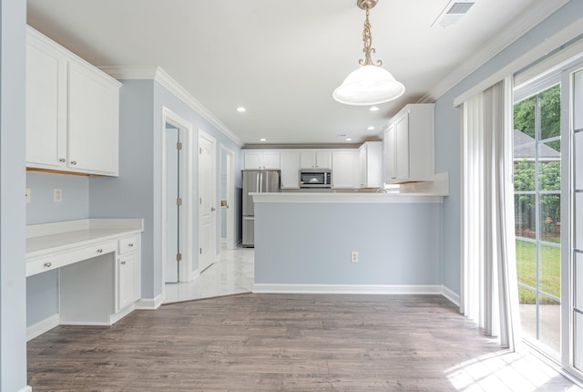 kitchen with crown molding, stainless steel appliances, built in desk, white cabinets, and decorative light fixtures