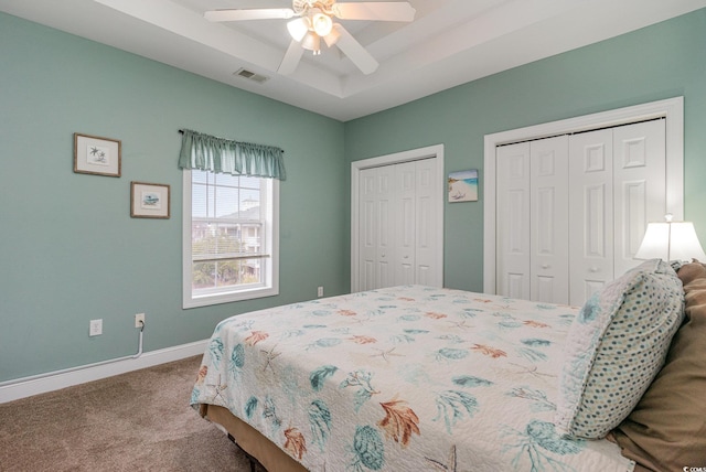 carpeted bedroom featuring a tray ceiling, two closets, visible vents, ceiling fan, and baseboards