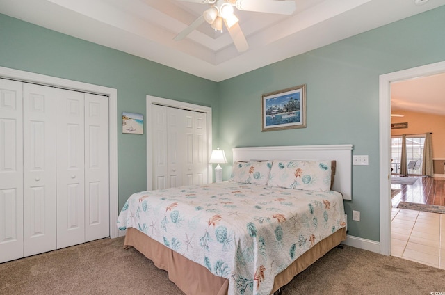 bedroom featuring carpet floors, two closets, a raised ceiling, ceiling fan, and tile patterned flooring