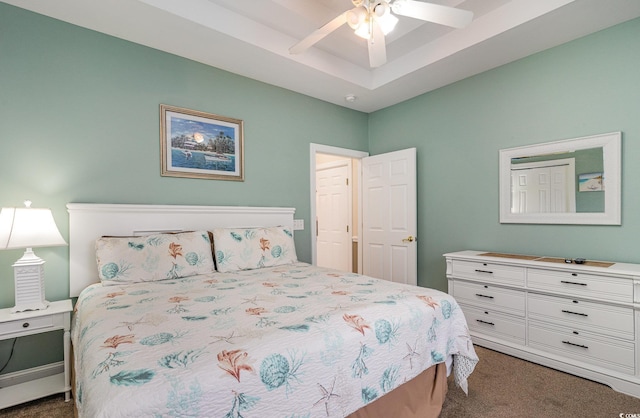 bedroom with a ceiling fan, dark carpet, and a tray ceiling