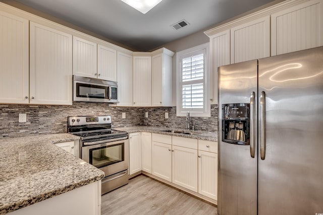 kitchen featuring sink, light hardwood / wood-style floors, decorative backsplash, light stone countertops, and appliances with stainless steel finishes