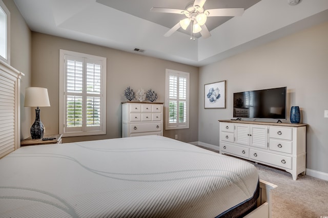 bedroom featuring ceiling fan, multiple windows, and a raised ceiling