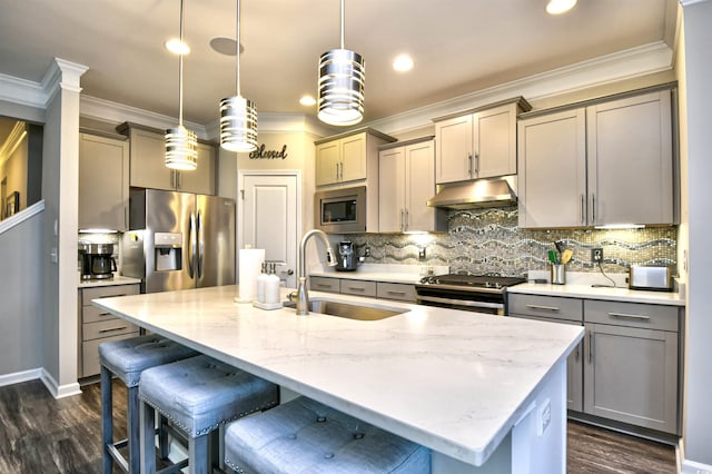 kitchen featuring sink, appliances with stainless steel finishes, hanging light fixtures, light stone counters, and a center island with sink