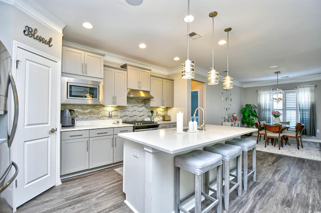 kitchen featuring a breakfast bar area, gray cabinets, appliances with stainless steel finishes, hanging light fixtures, and a center island with sink