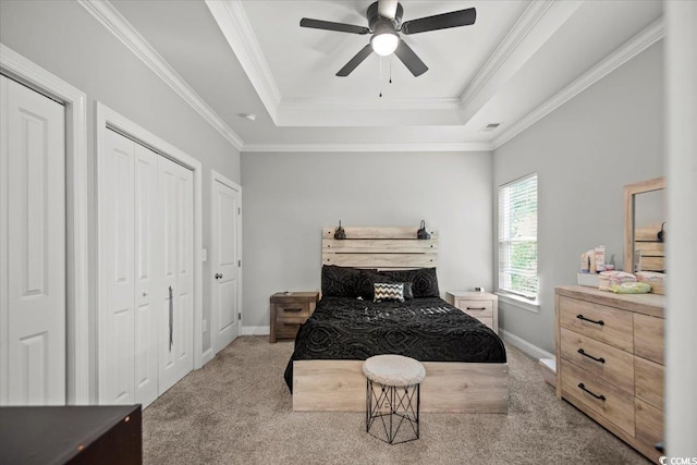 carpeted bedroom with ceiling fan, a tray ceiling, crown molding, and multiple closets