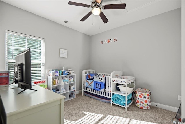 bedroom featuring ceiling fan, a nursery area, and carpet floors