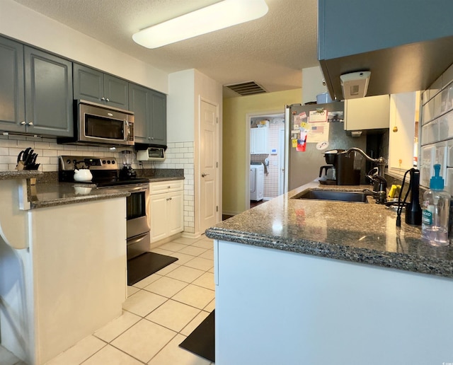 kitchen with a textured ceiling, washing machine and dryer, stainless steel appliances, sink, and light tile patterned floors