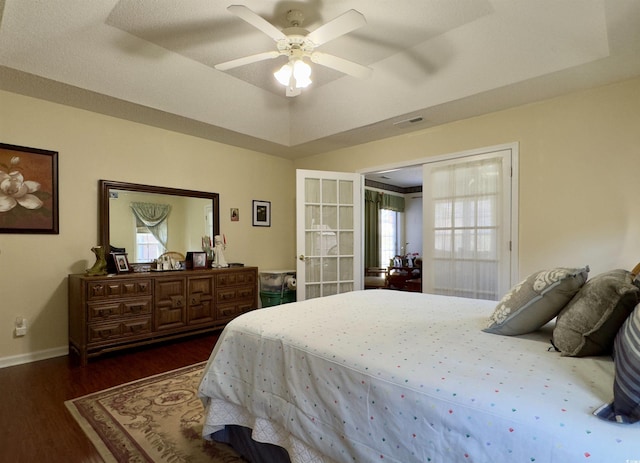 bedroom featuring ceiling fan, french doors, dark hardwood / wood-style flooring, and a tray ceiling