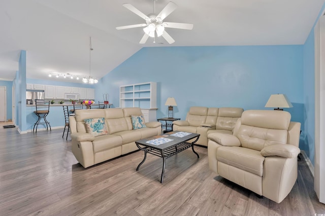 living room featuring ceiling fan with notable chandelier, vaulted ceiling, and light hardwood / wood-style floors