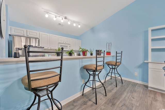 kitchen with white cabinets, light hardwood / wood-style floors, a breakfast bar, and stainless steel fridge