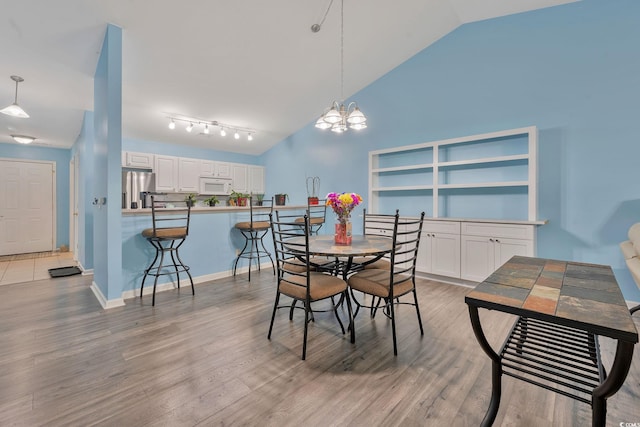 dining area with high vaulted ceiling, a notable chandelier, and light hardwood / wood-style flooring