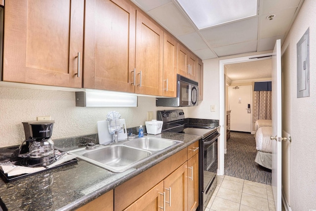 kitchen with black appliances, a paneled ceiling, light tile patterned floors, dark stone counters, and sink