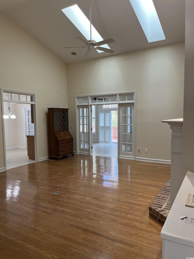 unfurnished living room with ceiling fan, hardwood / wood-style floors, high vaulted ceiling, and a skylight