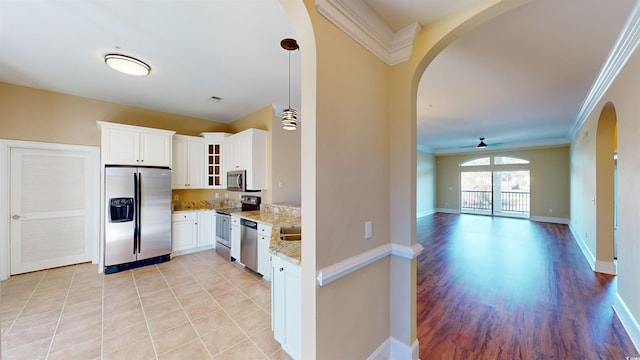 kitchen featuring arched walkways, appliances with stainless steel finishes, crown molding, glass insert cabinets, and light stone countertops