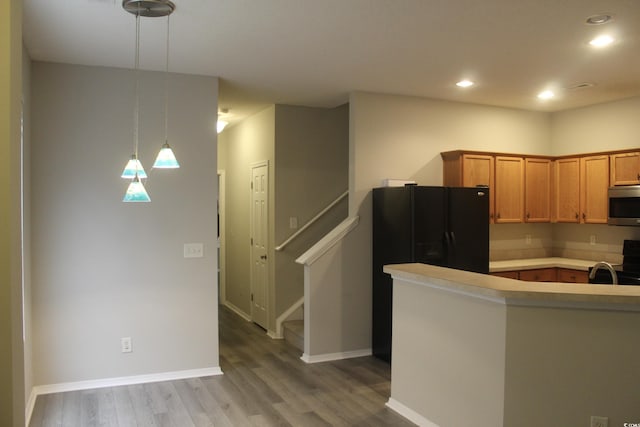 kitchen featuring light wood-type flooring, stainless steel appliances, kitchen peninsula, and decorative light fixtures