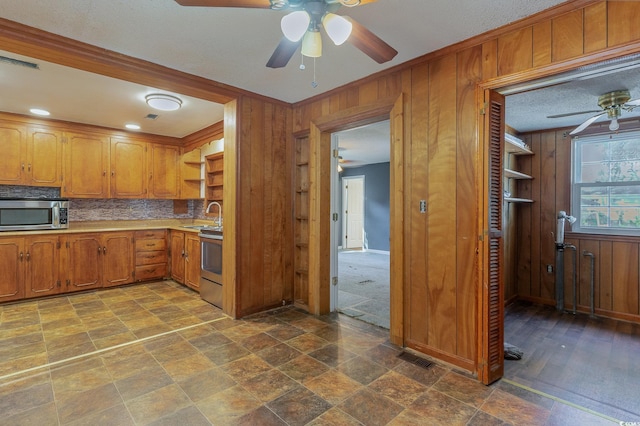 kitchen featuring sink, tasteful backsplash, appliances with stainless steel finishes, wooden walls, and ceiling fan