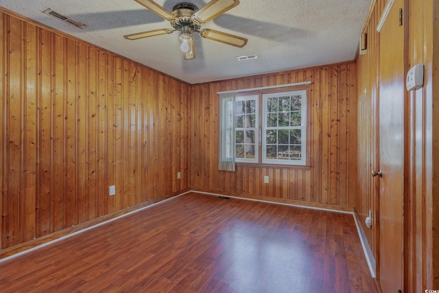 unfurnished room featuring ceiling fan, dark wood-type flooring, a textured ceiling, and wood walls