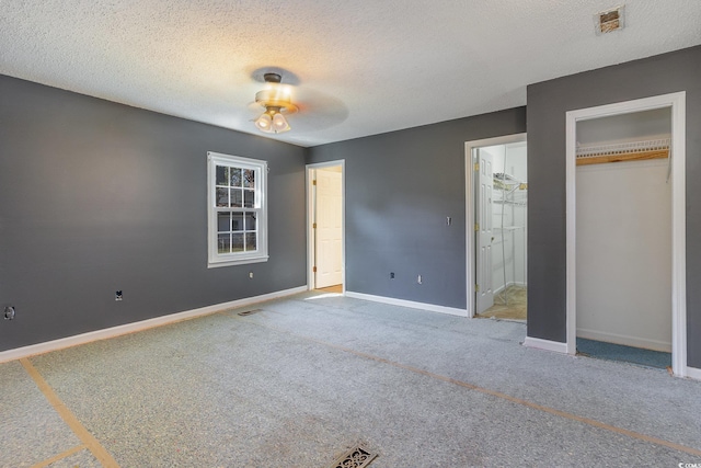 unfurnished bedroom with a closet, connected bathroom, carpet flooring, and a textured ceiling