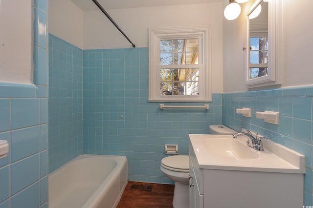 full bathroom featuring tile walls, hardwood / wood-style flooring, vanity, toilet, and washtub / shower combination